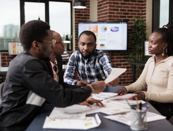 Startup employees doing teamwork to plan project, analyzing information and data on documents. Using laptop and paperwork files to do research and create corporate presentation in office.
